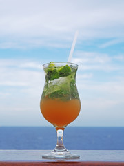 Mojito cocktail with lime and mint on a background of sea, sky with clouds. 