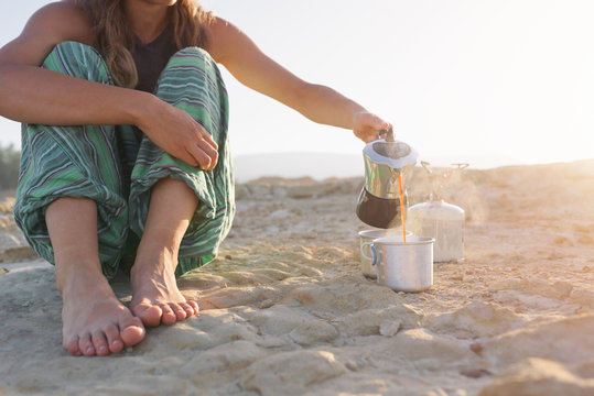Woman sat on the golden sand pouring coffee in a cup
