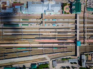 Aerial photography of a modern railroad tracks, trains with wagons on parallel railways, crossings, a railway station, high-rise buildings, a bridge across the river on a warm summer day. 
