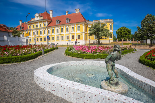 View of a water fountain with statue and flowers in a park with the City museum located in the Eltz castle in the background  in Vukovar, Croatia.