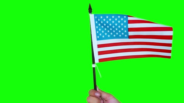 American Independence Day Concept. Male hand holds waving American flag over green screen background in studio