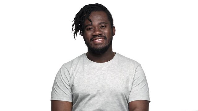 Portrait of big african american man with afro hairdo in casual t-shirt greeting with waving hand on camera with smile, isolated over white background. Concept of emotions