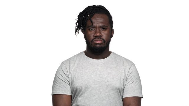 Portrait of severe bearded dark skinned guy in casual t-shirt with strict gaze asking to keep quiet putting index finger on lips, isolated over white background. Concept of emotions