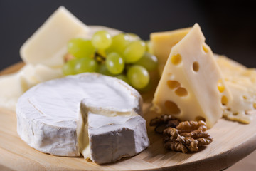 Fototapeta na wymiar Different kinds of cheese on a plate with grapes and nuts