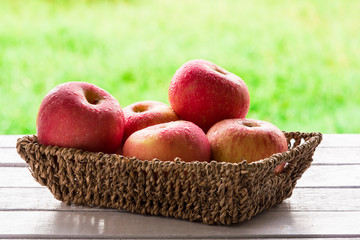 Red apples in basket on wooden table with natural green background