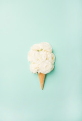 Flat-lay of waffle sweet cone with white buttercup flowers over light blue pastel background, top view, vertical composition. Spring or summer mood concept