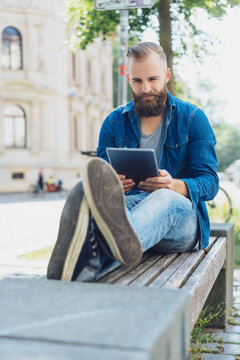 Young man on city park bench using tablet
