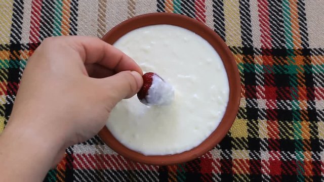 Dipping strawberry in yogurt and eating it.