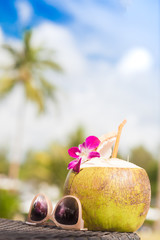 Fresh coconut cocktail decorated with orchid flower and sunglasses on a tropical beach