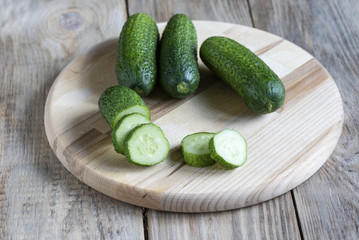 Three whole fresh cucumber and slices of cucumber on a cutting b