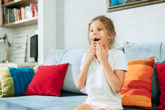 Little surprised teen girl watching tv at home.