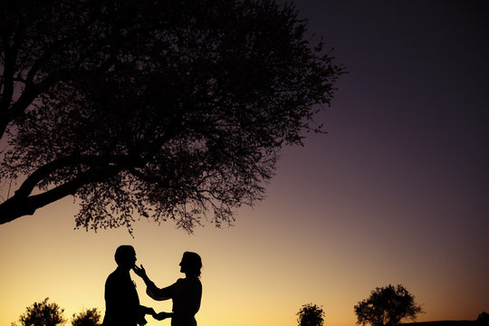 Silhouette of bride caressing groom at dramatic sunset surrounded by trees