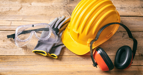 Construction safety. Protective hard hat, headphones, gloves and glasses on wooden background