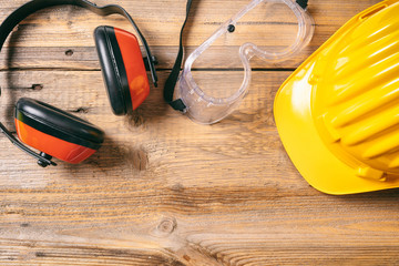Construction safety. Protective hard hat, headphones and glasses on wooden background, copy space, top view