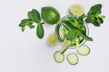 Cooking fresh summer organic lemonade with slices cucumber, ice, lime, mint, straw on white wood background, top view, closeup. Healthy detox fresh water.