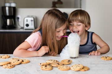 Laughing kids making mess while blowing bubbles in glass of milk