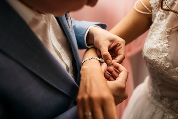 The groom fastens the bracelet on the bride's wrist - obrazy, fototapety, plakaty