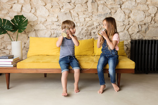 Siblings playing with tin can telephone on yellow sofa