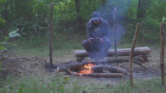 A freelancer man touch a tablet near tourist campfire in evening
