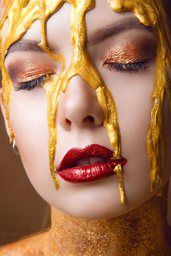 A glamorous portrait of a girl with professional make-up on closed eyes and spread gold paint on her face close-up.