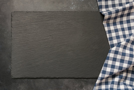 Black slate background with kitchen blue checkered towel. Cooking food, picnic or food background with copy space. Top view.