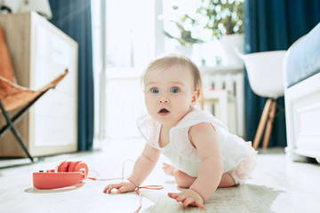 Fototapeta premium Cute young baby sitting on the floor at home playing with headphones