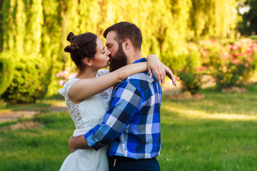 Fototapeta premium Beautiful guy and girl hugging and kissing. Love story photo on outdoor in sunset light. Couple in love. Pretty girl and brutal bearded guy in outdoor.