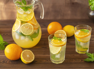 Lemonade drink sparkling water, lemon, orange and mint leaves in a jug on a wooden background.