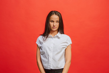 The serious business woman standing and looking at camera against red background.