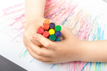 Drawing on a white sheet of paper with colored wax pencils. The concept of children's creativity and hobbies. The child draws a set of colored pencils abstract lines and patterns. Baby hands closeup