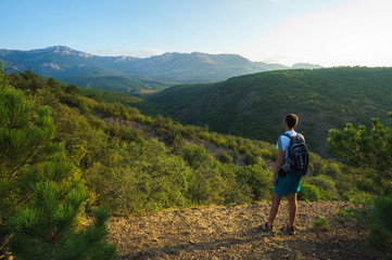 Fototapeta premium A young man stands on the edge of a rock and looks into the distance to the Crimean mountains. The Landscape Of Russia. Photo of a tourist.