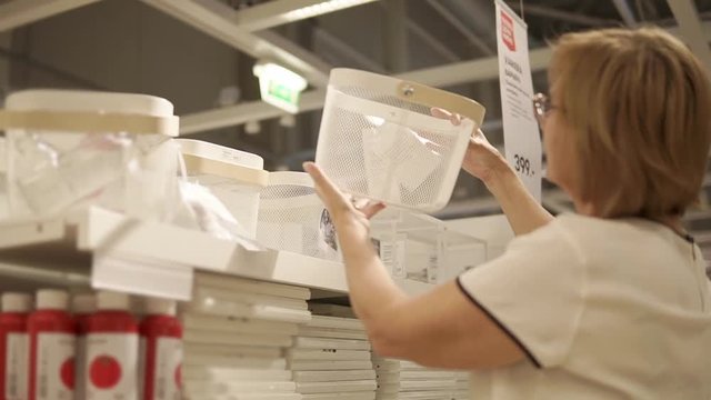 Close up shot of a blonde woman taking box off the shelf in a store. Woman buys box for cutlery in a household store. She likes the desing and smiles.