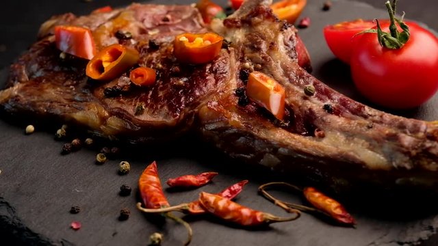 Close-up of grilled beef steak on bone with tomatoes rotating on the stone cutting board
