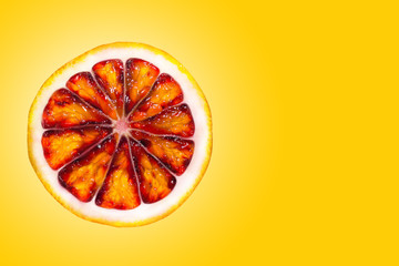 Top view of textured ripe slice of red orange citrus fruit isolated on yellow background....