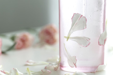 A Pink perfume bottle with pink and white carnation flowers and petals.
