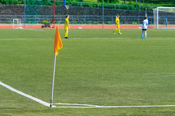 Fototapeta na wymiar Yellow corner flag on the football field against a players in blur