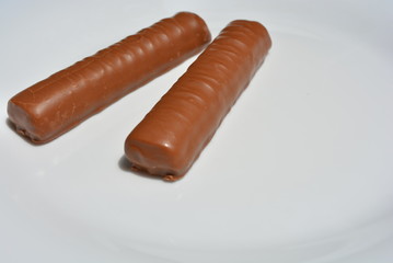 On a white plate of glass are two chocolate bars with a sandy liver and caramel, covered with a layer of milk chocolate