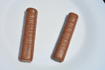 On a white plate of glass are two chocolate bars with a sandy liver and caramel, covered with a layer of milk chocolate