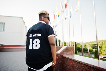 Stylish arabian muslim boy with originally hair posed on streets, against flags of different countries.
