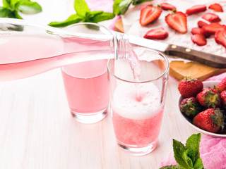 Glasses of a fresh pink lemonade. Strawberry soda on a wooden table. Pouring a soda from a bottle