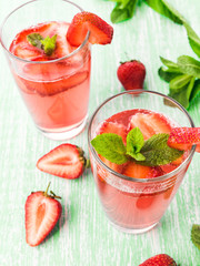 Glasses of a fresh pink lemonade. Strawberry soda with mint on a wooden table. 