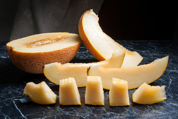 Half and sliced honeydew melon fruit on dark marble background..