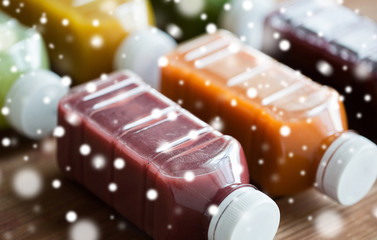 healthy eating, drinks, diet and packaging concept - close up of plastic bottles with different fruit or vegetable juices on wooden table over snow
