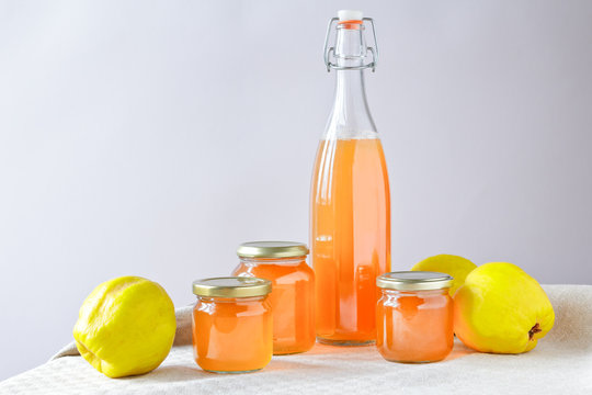 Homemade quince jelly and Juice in a bottle and glass jars with quinces on a linen tablecloth in front of a neutral background, copy space