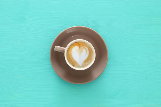 image of coffe cup with foam of heart shape over wooden blue table.
