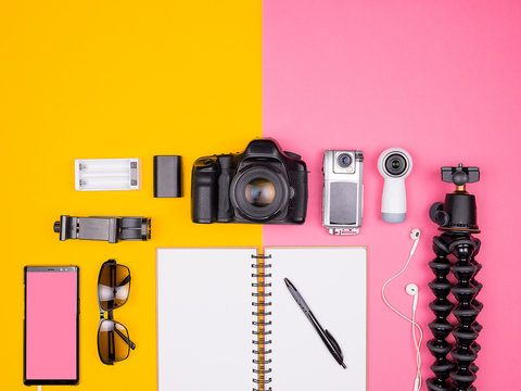 Blogger ready for travel and summer vacation. Top view. Flat lay. 360, DSLR and action camera, sunglasses, smartphone, paper notebook and passport on two colored background. Pastel colors