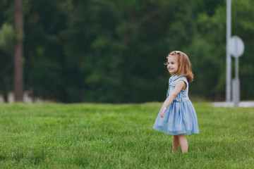 Pretty little cute child baby girl in denim dress standing, play and have fun on green grass lawn in park. Mother, little kid daughter. Mother's Day, love family, parenthood, childhood concept.