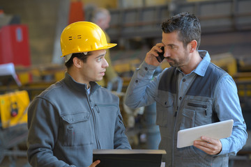male supervisor talking on mobile phone with worker at industry - obrazy, fototapety, plakaty