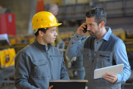 male supervisor talking on mobile phone with worker at industry
