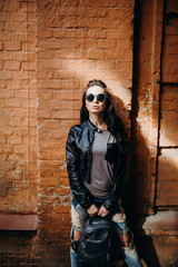 Attractive young woman walking outdoors. Close up fashion woman, vintage denim biker leather jacket, rocknroll style, fit girl posing on street, stylish outfit. On the background of red brick wall.